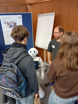 Zwei Menschen von hinten schauen sich einen kniehohen Roboter an